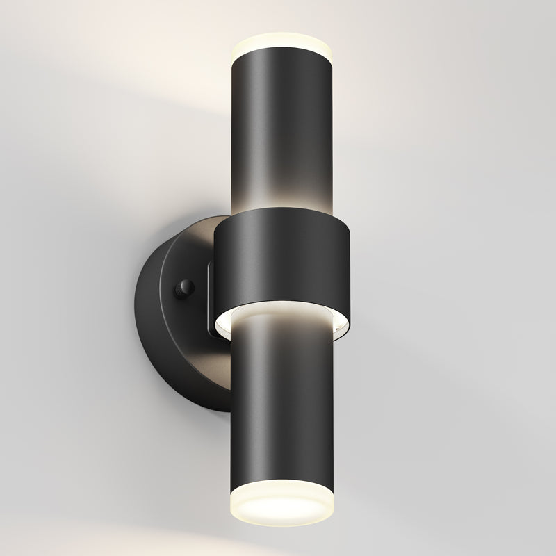 The Artika Dani modern LED indoor-outdoor wall light 5 CCT is a sleek black cylindrical sconce with up-and-down lights on a round base, shown mounted on a light-colored wall.