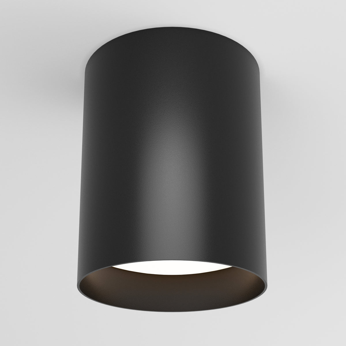 A modern, cylindrical black ceiling light fixture is mounted on a white ceiling. The fixture has a smooth surface and emits soft white light from its open bottom.