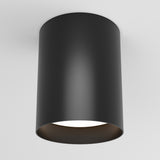 A modern, cylindrical black ceiling light fixture is mounted on a white ceiling. The fixture has a smooth surface and emits soft white light from its open bottom.