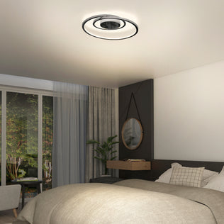 Modern bedroom with an Artika Salto LED flush mount light, large bed, grey accent wall, round mirror above a floating wooden shelf, potted plant, and floor-to-ceiling windows overlooking lush greenery.