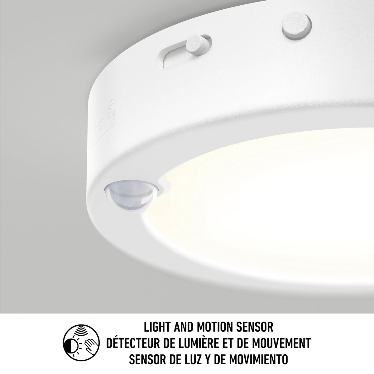 Close-up of a round white ceiling light with a built-in light and motion sensor. Text below in English, French, and Spanish reads: Light and motion sensor / Détecteur de lumière et de mouvement / Sensor de luz y de movimiento.