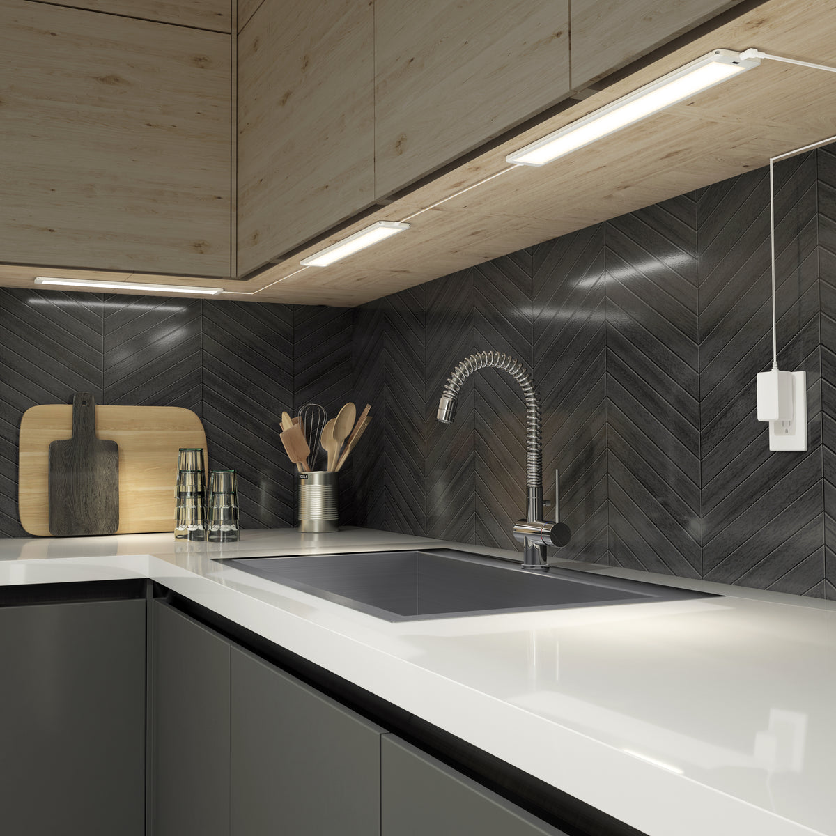 Modern kitchen featuring a dark chevron backsplash, white countertop, Artika’s Maestro under cabinet LED light 3CCT, sleek faucet, kitchen utensils in a holder, two glasses, and cutting boards against the backsplash.