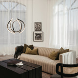 A modern living room with a striped beige sofa, green pillows, a black wooden coffee table, and abstract wall art. Sheer curtains cover large windows, and a sculptural pendant light hangs from the ceiling.