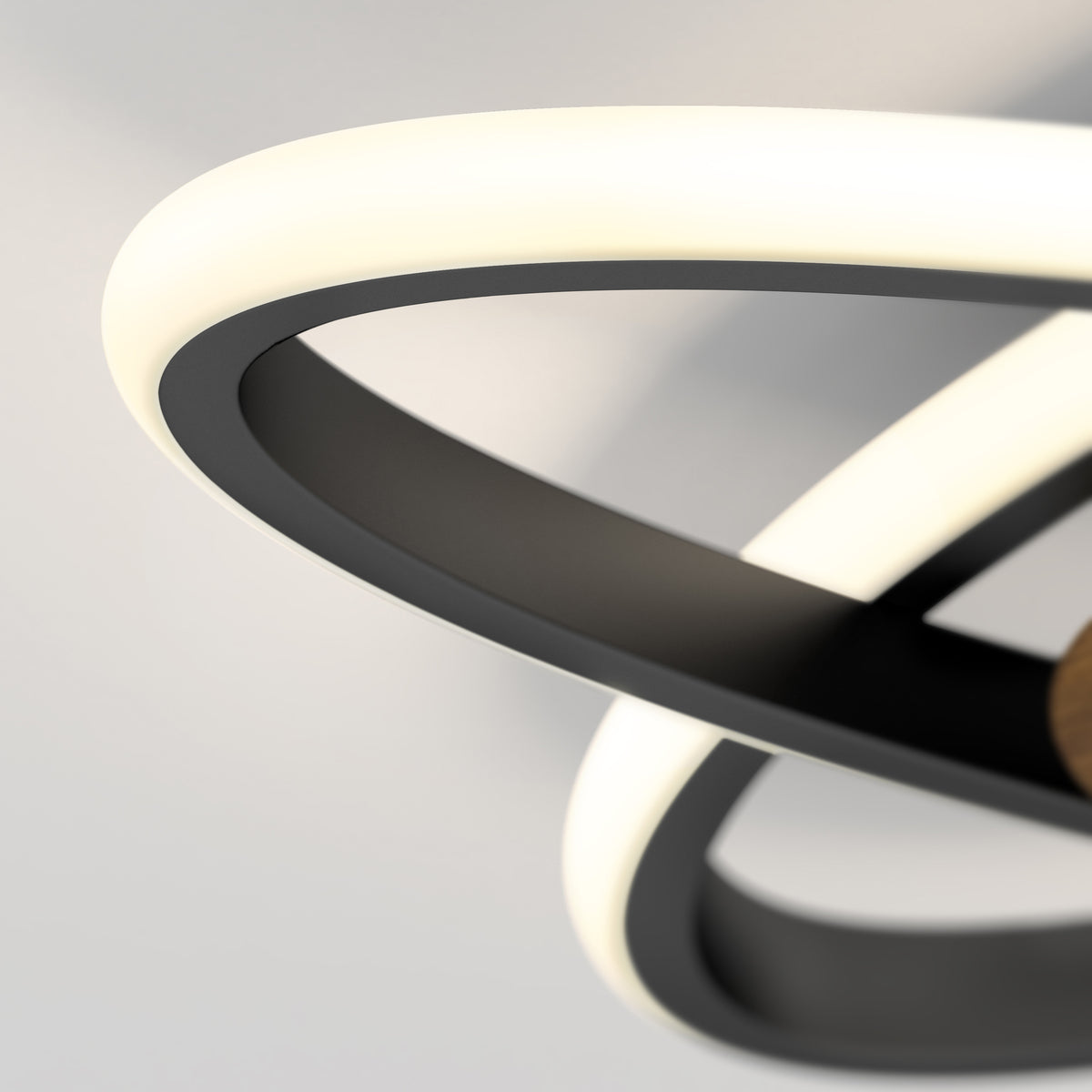 Close-up of a modern ceiling light fixture with intertwined black and white illuminated rings, set against a plain light-colored background.