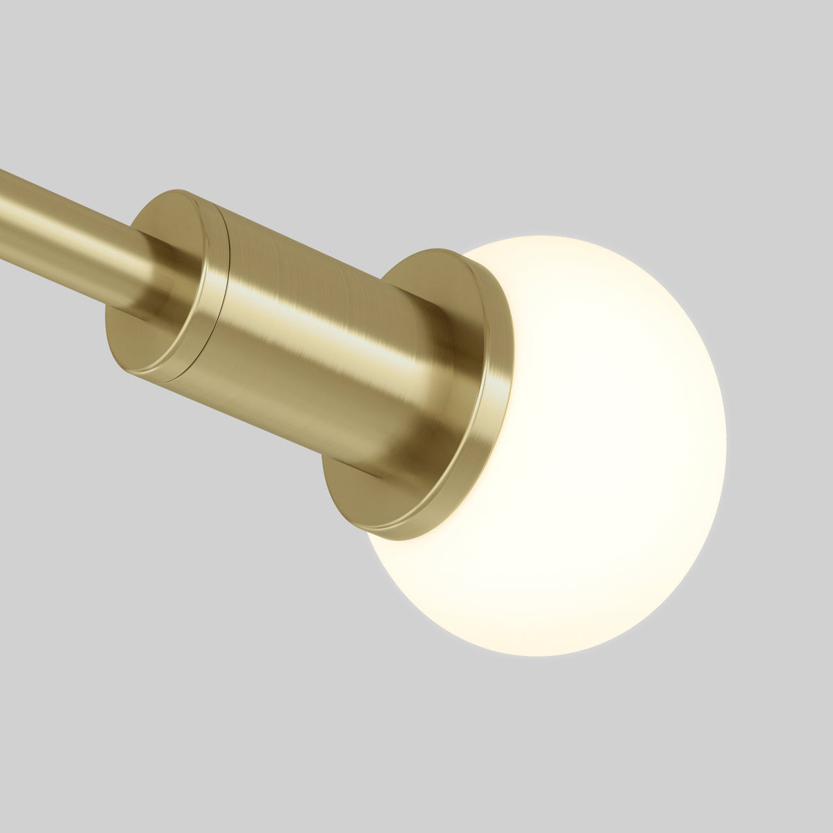 A close-up of a modern brass light fixture with a cylindrical arm and a round, frosted glass bulb, set against a plain gray background.
