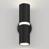 A modern black cylindrical wall sconce with vertical grooves emits light from the top and bottom, mounted on a plain white wall.