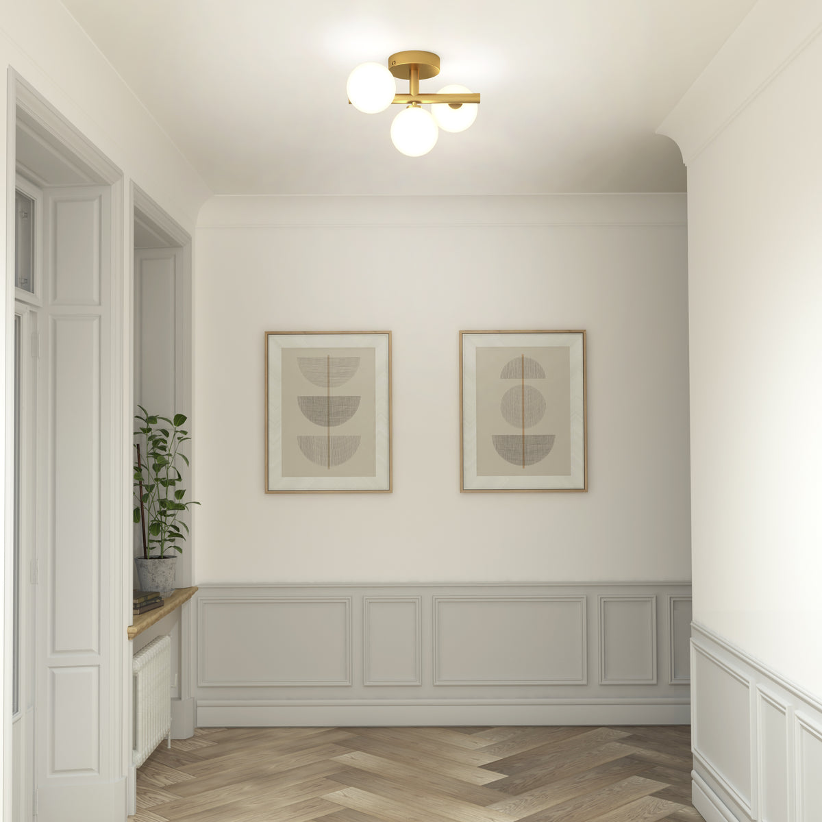 A hallway with light gray wainscoting, herringbone wood floor, two framed abstract art prints on the wall, a gold and white ceiling light, and a potted plant on a windowsill.
