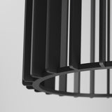 Close-up of a black, modern, geometric metal lampshade with vertical bars and a circular base against a light gray background.