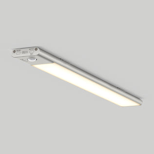 The Artika Outline under cabinet LED light 3CCT is a slim, rectangular fixture with a silver metallic frame and soft white illumination, featuring visible control buttons and mounted on a plain light gray ceiling.