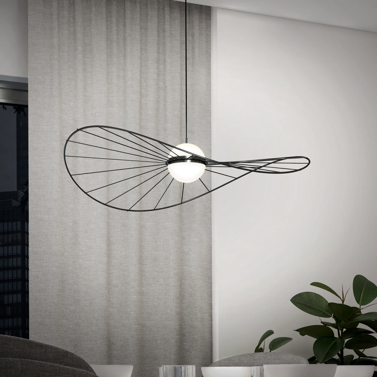 A modern pendant light with a sculptural, black wire frame and two white globes hangs in a minimalist room with light gray curtains, a window, and a green potted plant.