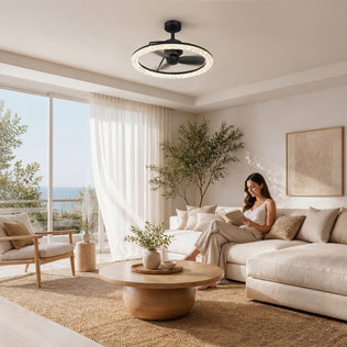 A woman reads on a beige sofa in a bright living room with a round table and the Artika Carat 23" LED Modern Ceiling Fan with remote.