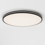 A modern, round ceiling light fixture with a black rim and a smooth white surface, mounted on a plain white ceiling.