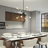 Modern kitchen and dining area with a white table set for six, wooden chairs, minimalist gray cabinets, wood accents, and a contemporary chandelier hanging above. Large window lets in natural light.