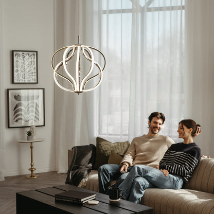 A couple sits on a cozy sofa in a modern living room with large windows, sheer curtains, framed artwork, and the Artika Meridian LED pendant light overhead. Smiling and relaxed, they sit by a coffee table.