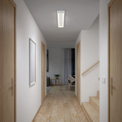 A modern hallway features light wood doors, stairs on the right, and a wooden floor. An Artika Aiden 48 in. LED modern flush mount light 5 CCT brightens the space. At the end is a room with a chair, table, plant, and sheer curtains.
