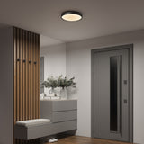 A modern entryway with a gray door, wooden slat divider, built-in bench, floating drawers, and a vase of greenery. A round ceiling light illuminates the space with a warm glow.