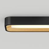 A modern rectangular wall light fixture with a black outer frame, wooden inner lining, and a soft white glow, mounted on a light grey wall.
