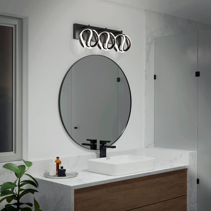 Modern bathroom with a round mirror above a rectangular sink, black faucet, wooden vanity, and decorative toiletries. Overhead, the Artika Vivaldi LED contemporary bathroom vanity light 3 CCT adds style. A green plant sits in the foreground.