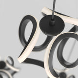 Close-up of a modern, abstract black and white LED pendant light fixture with curved, looped arms suspended from the ceiling against a plain, light gray background.